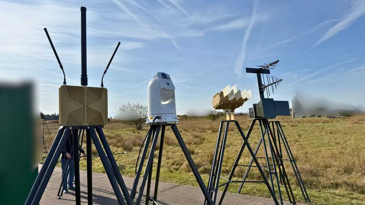 Counter-UAS sensors, a camera turret and RF antennas on tripods at the edge of an airfield